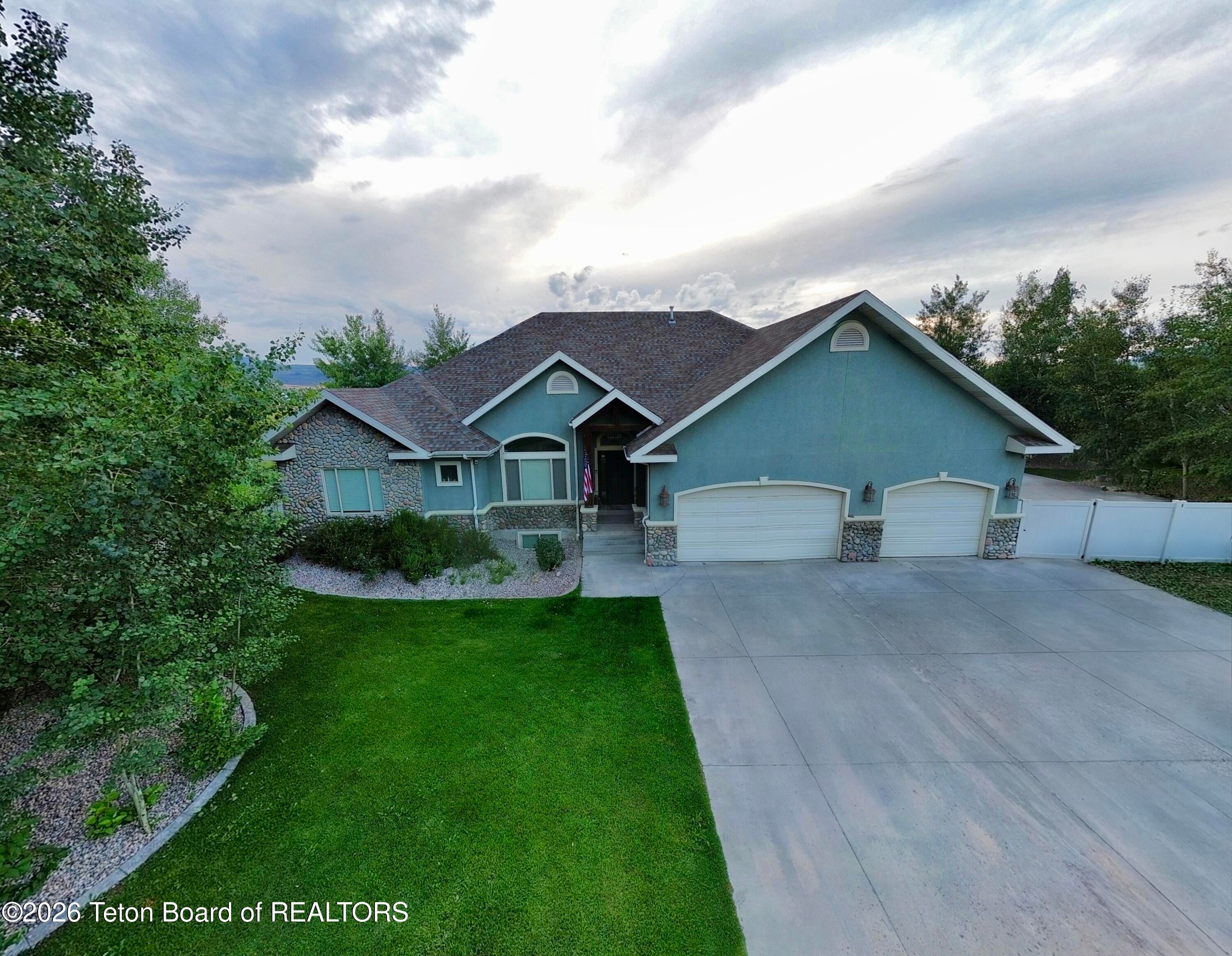 Blue single-story home with stone accents, a two-car garage, and a large front lawn under a cloudy sky. [AI-generated text]