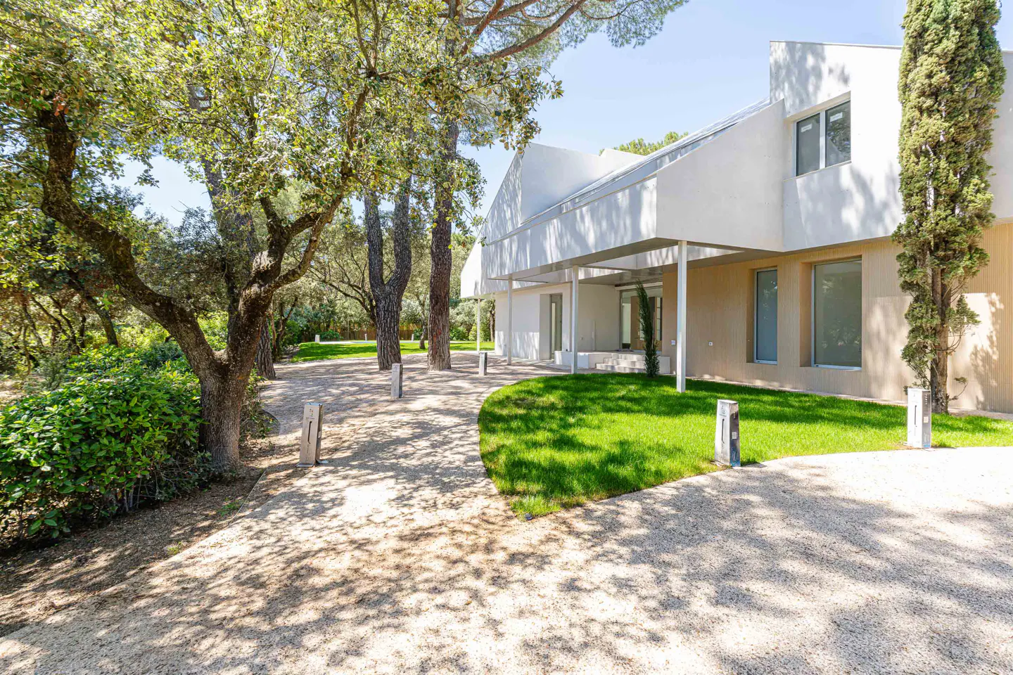 Modern white house with a gravel driveway, green lawn, and trees.