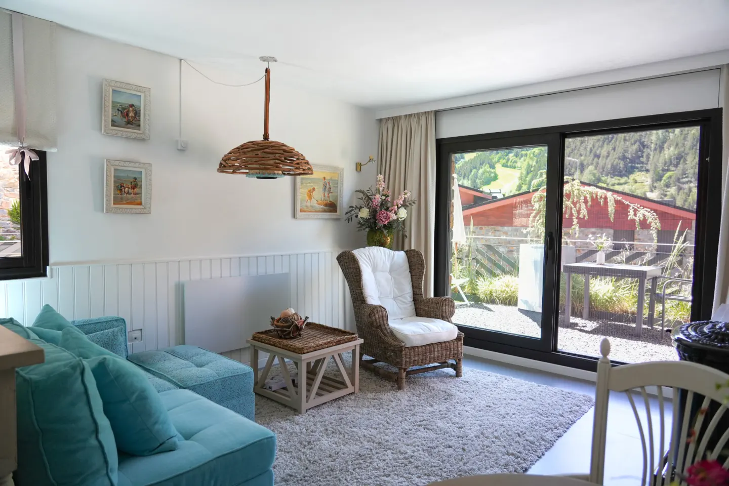 Bright living room with a turquoise sofa, wicker armchair, wooden coffee table, and sliding doors to a mountain view patio.