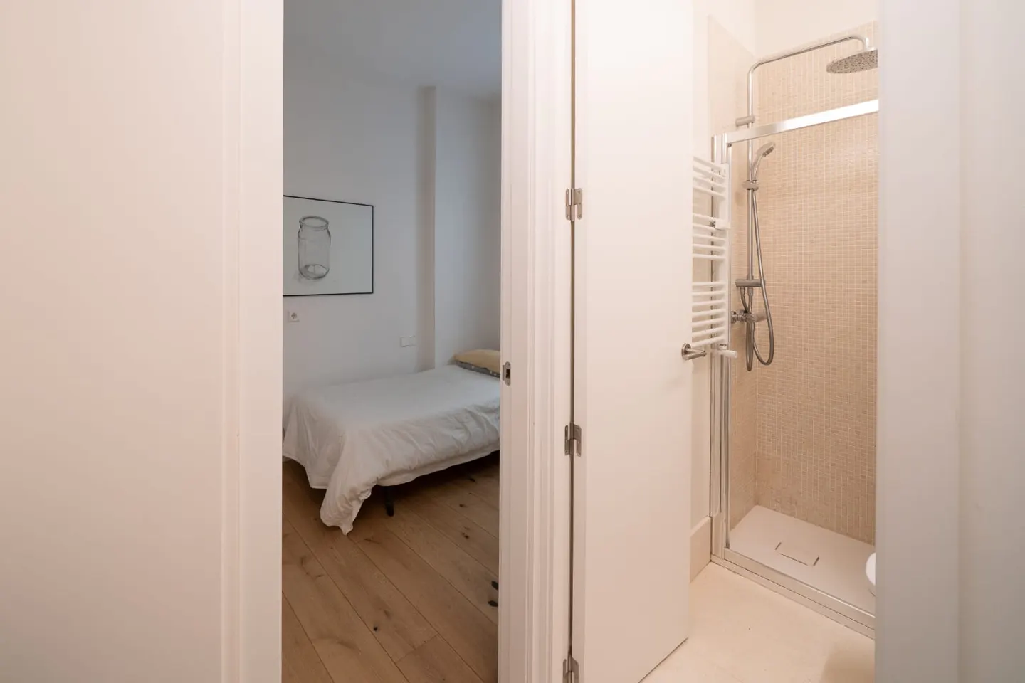 View through doorway of bedroom with bed and framed art, and bathroom with shower and towel rack.