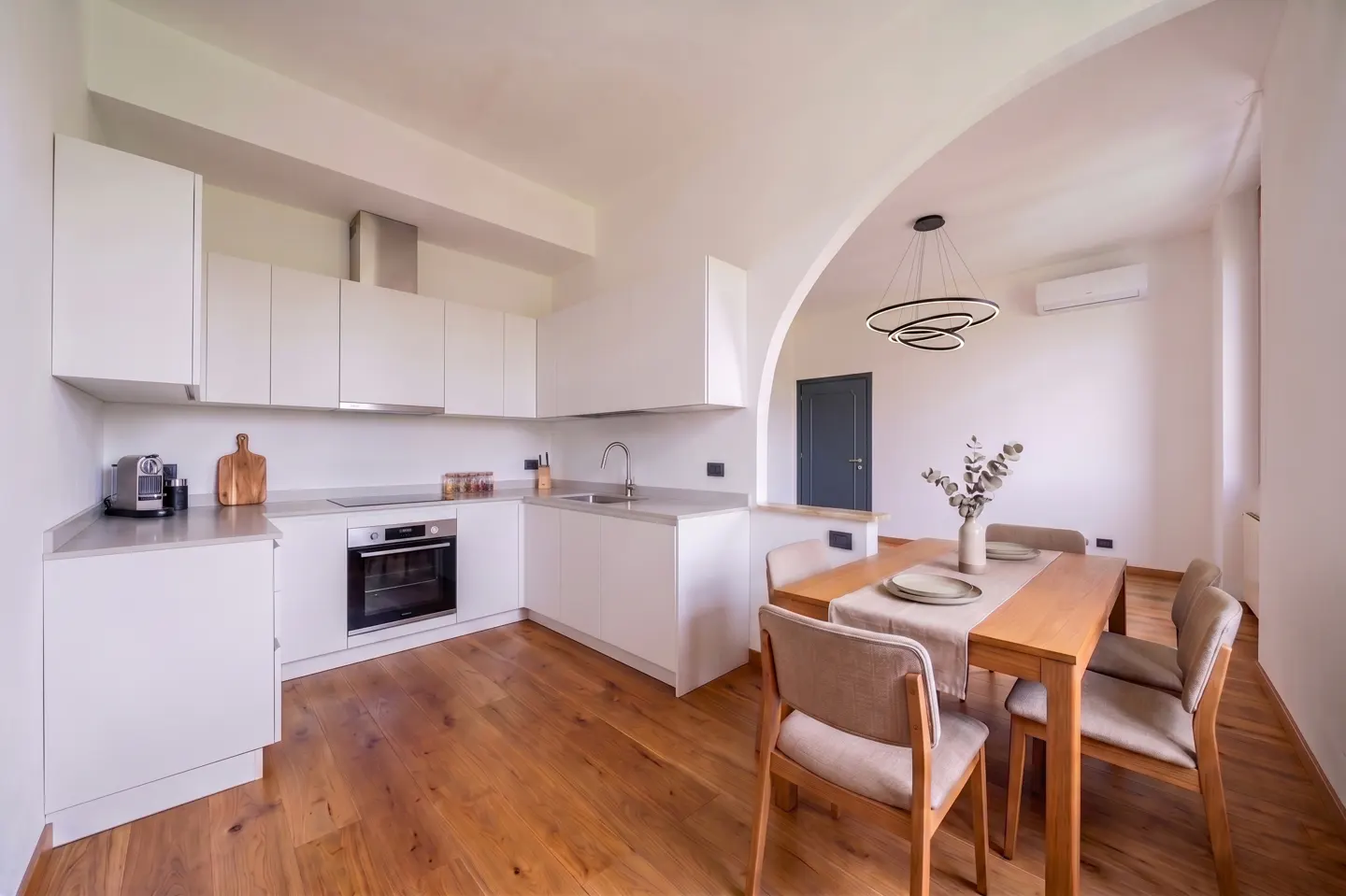 Bright, modern kitchen with white cabinets, stainless steel appliances, and a wood dining table set for four under a circular light fixture.