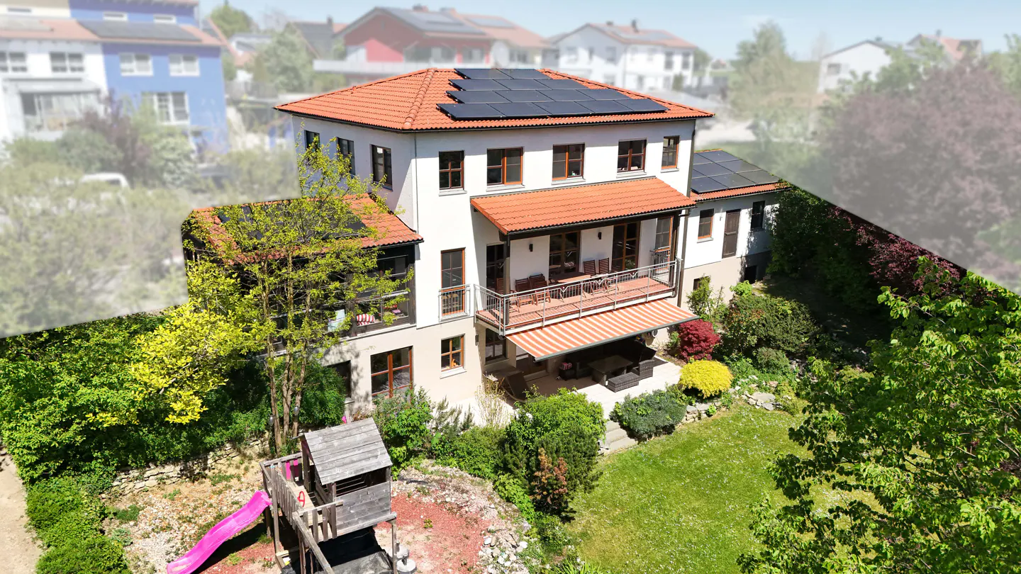Aerial view of a two-story white house with a red tile roof and solar panels, surrounded by a green lawn and trees. A wooden playset with a pink slide is visible.