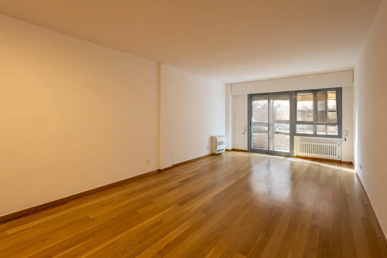 Empty room with hardwood floors, white walls, radiator, and sliding glass doors to a balcony.