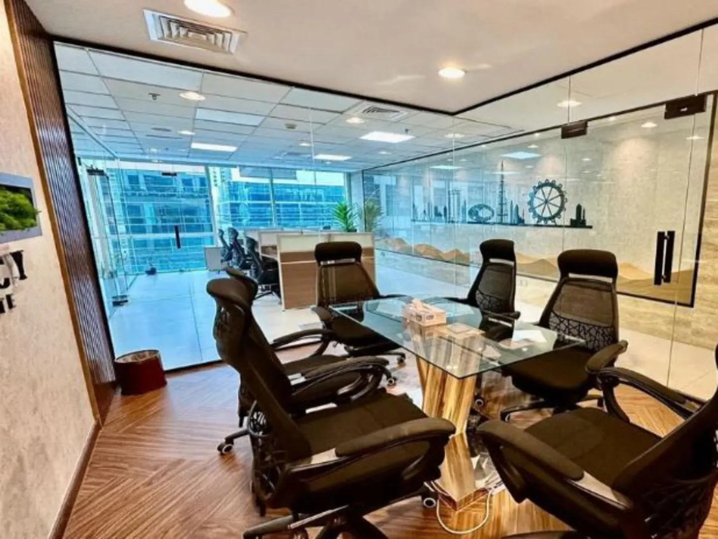 A modern office conference room with a glass table, black chairs, and a glass wall with a Dubai skyline design.