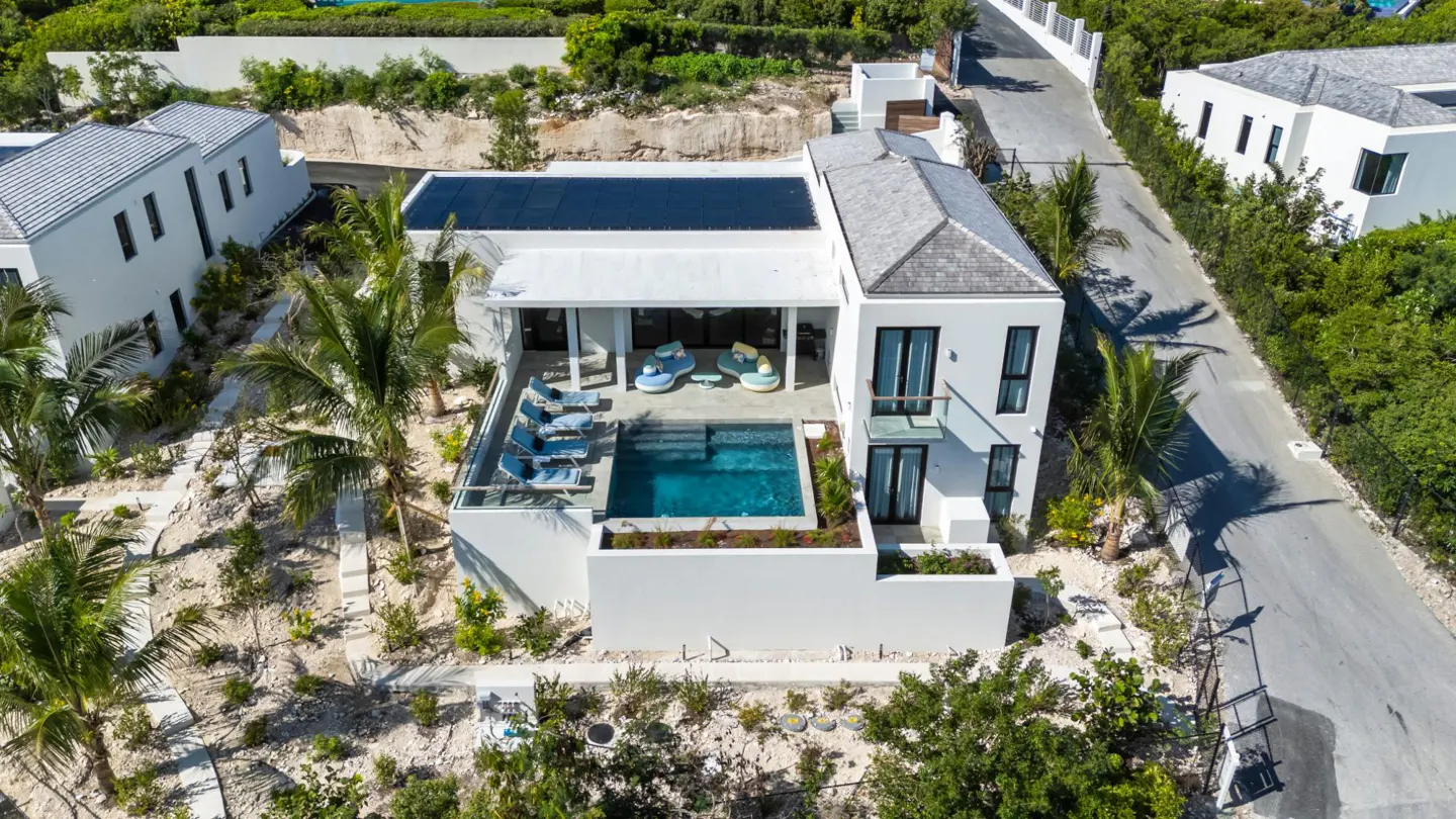 Aerial view of a modern white house with a pool, lounge chairs, and solar panels on the roof.