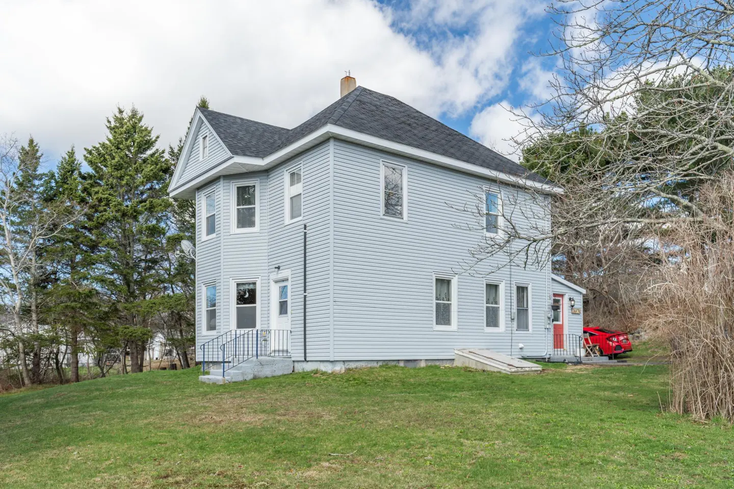 Two-story light blue house with a dark gray roof and white trim on a green lawn under a cloudy sky.