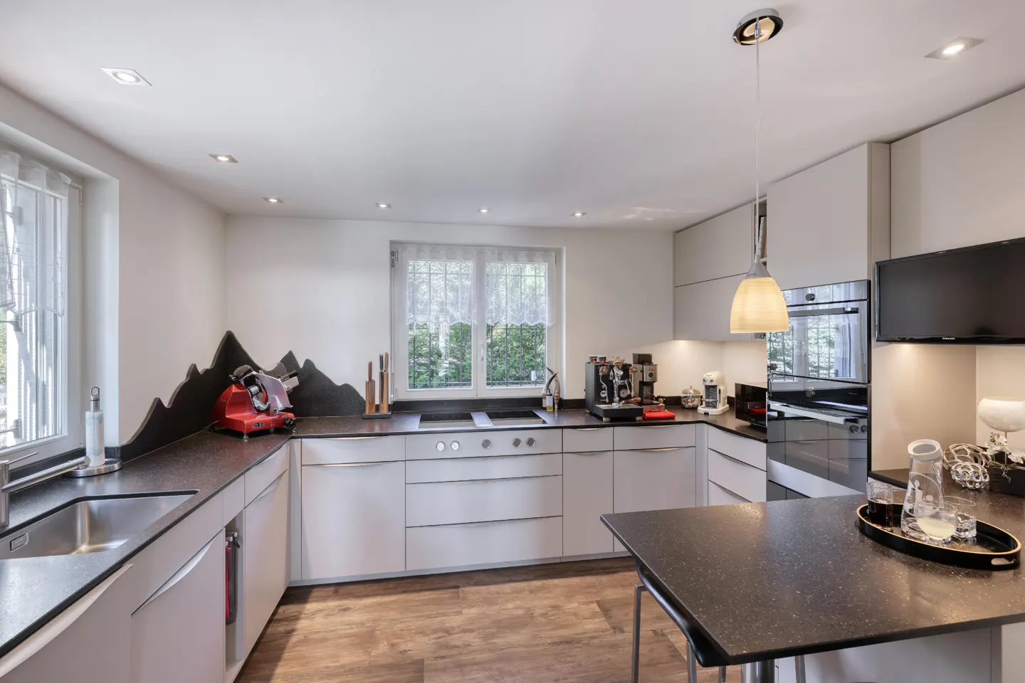 Bright kitchen with white cabinets, dark countertops, and wood-look flooring. A mountain-shaped backsplash adds a unique touch.