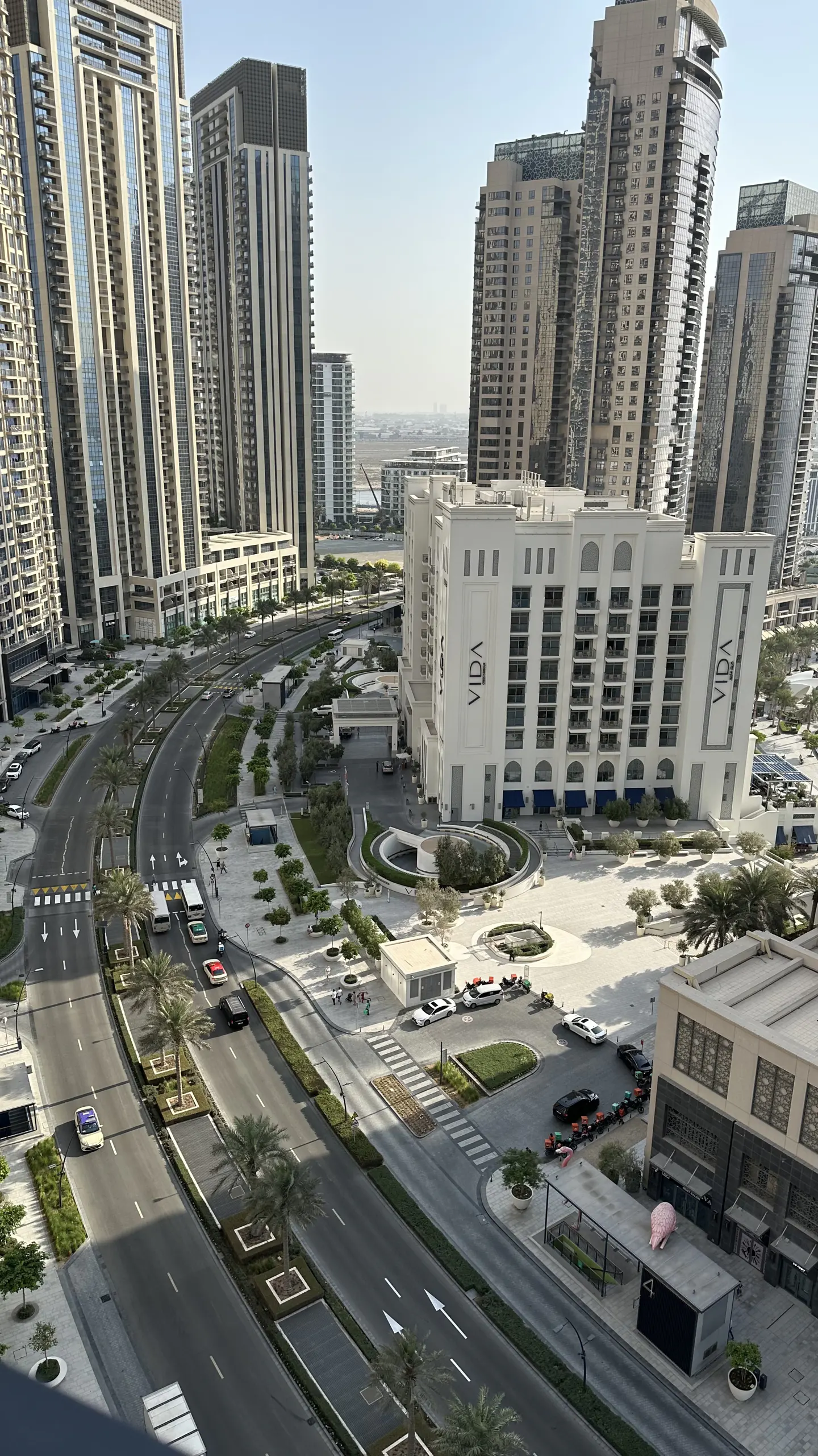 Cityscape view with tall buildings, roads, and a white VIDA hotel. Palm trees line the streets, and cars are visible on the roads.