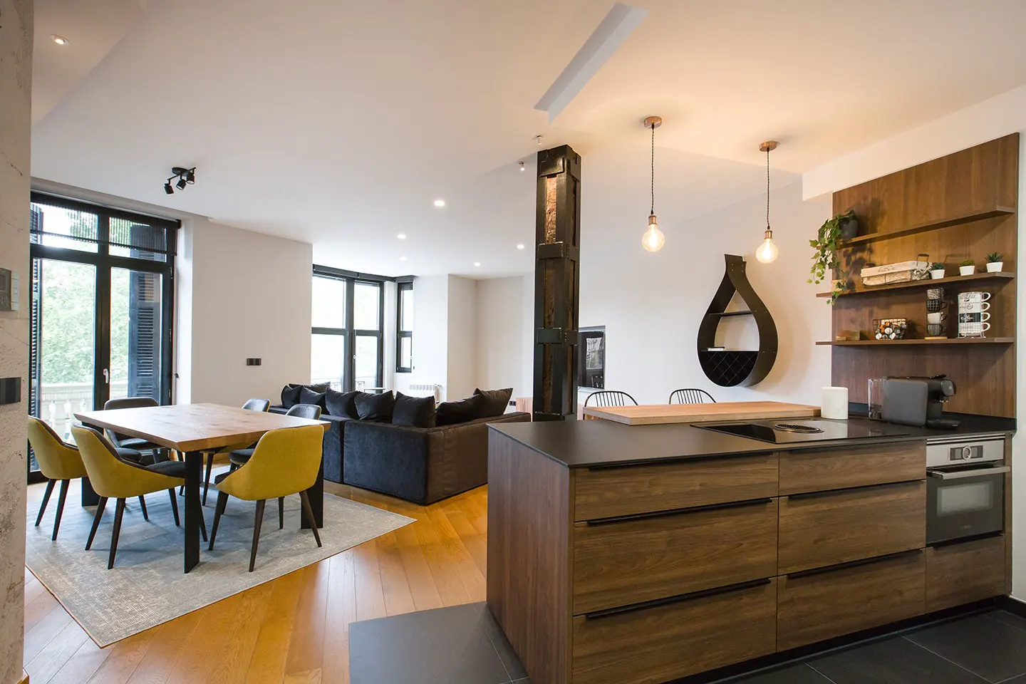 Open-concept living space with wood floors, a kitchen island, dining table with yellow chairs, and a gray sofa.