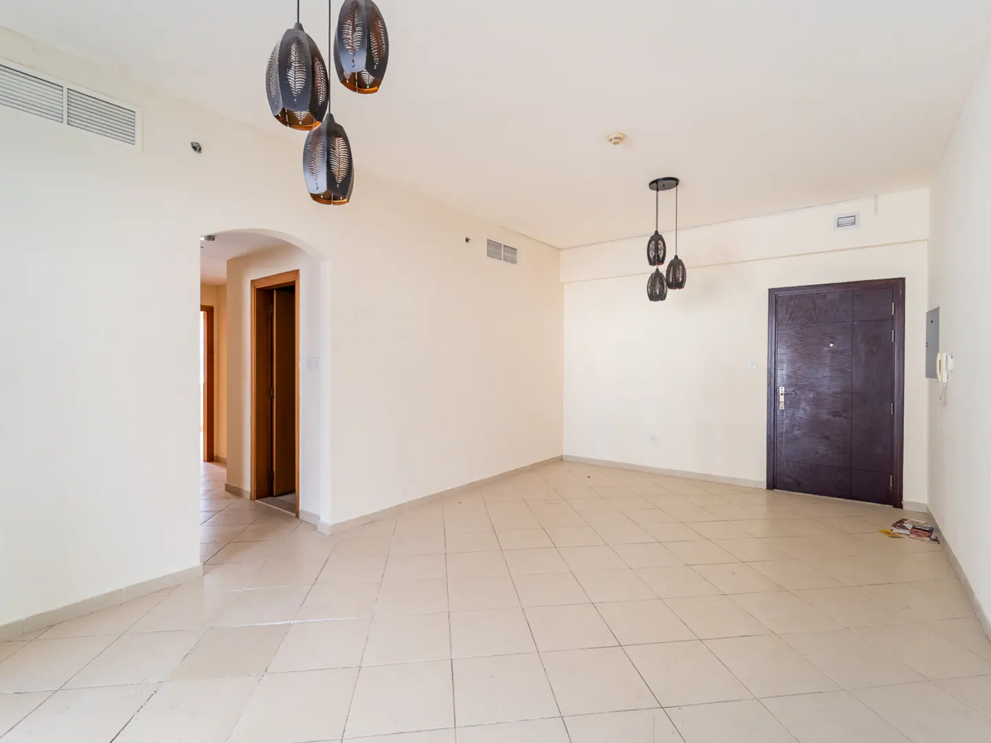 Empty room with beige tile flooring, white walls, and dark brown doors. Decorative pendant lights hang from the ceiling.