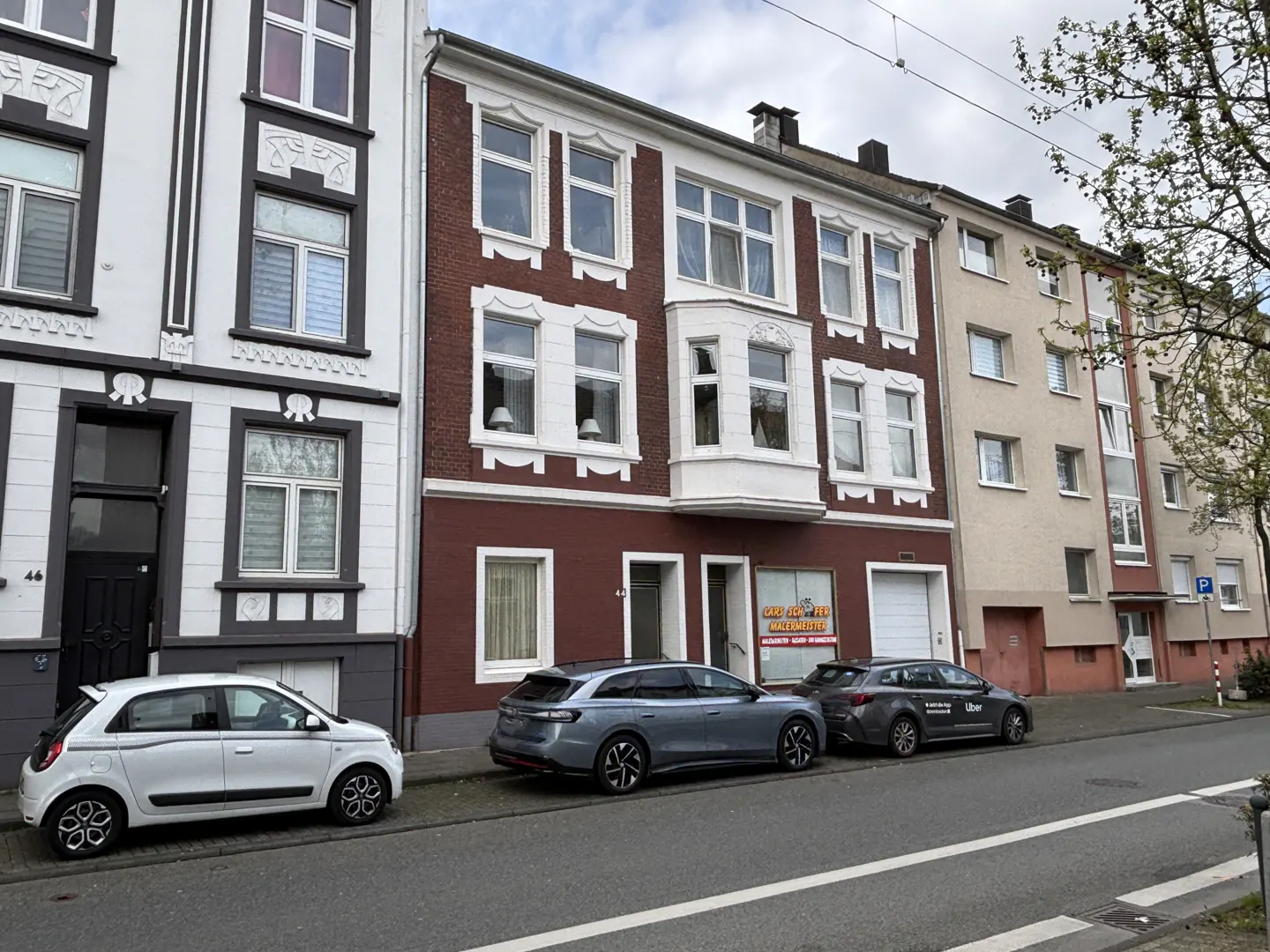 Street view of three-story buildings with parked cars. The building in the middle is red brick with white trim.