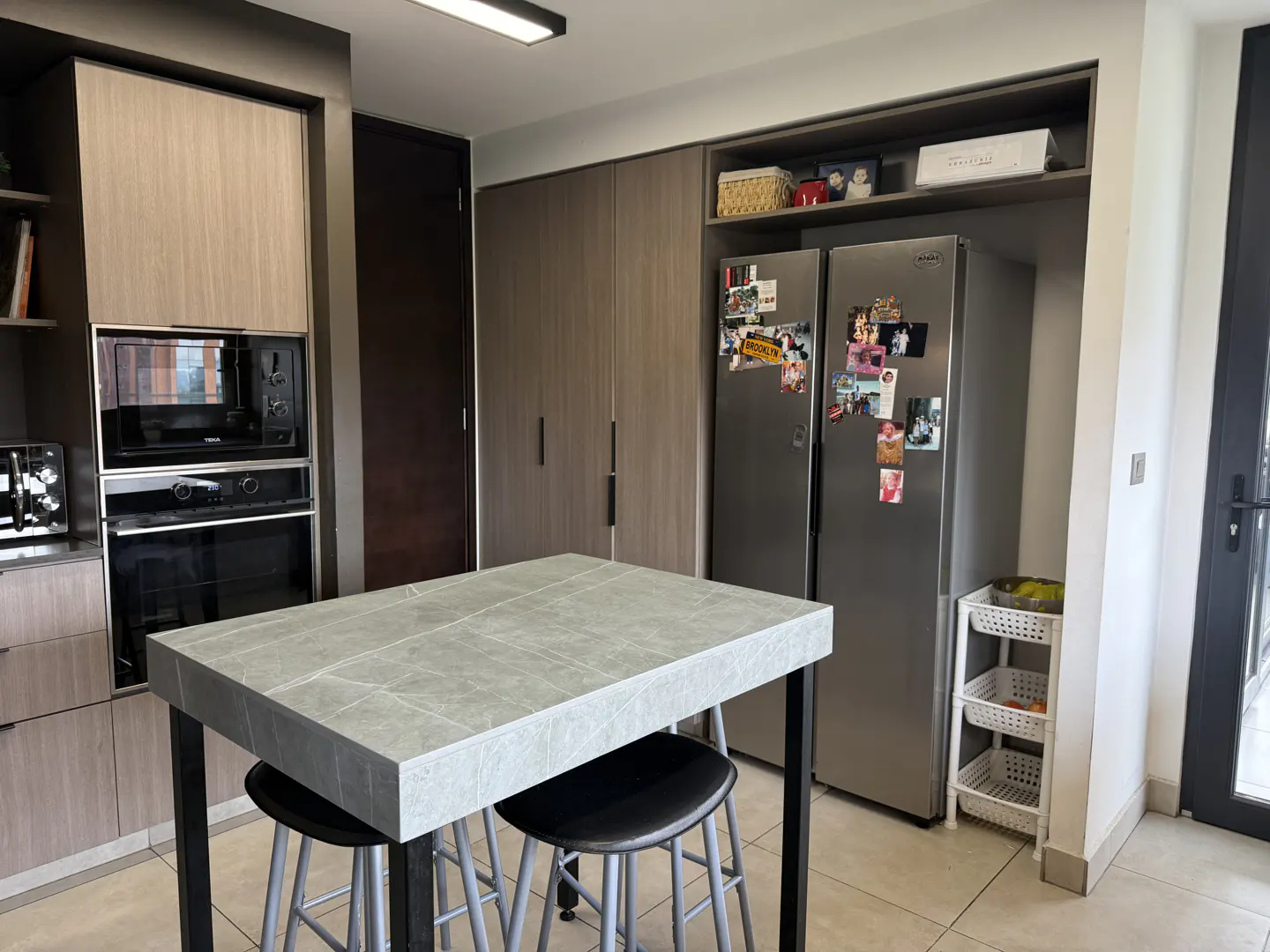 Modern kitchen with wood-grain cabinets, stainless steel appliances, a stone-topped island, and two black bar stools.