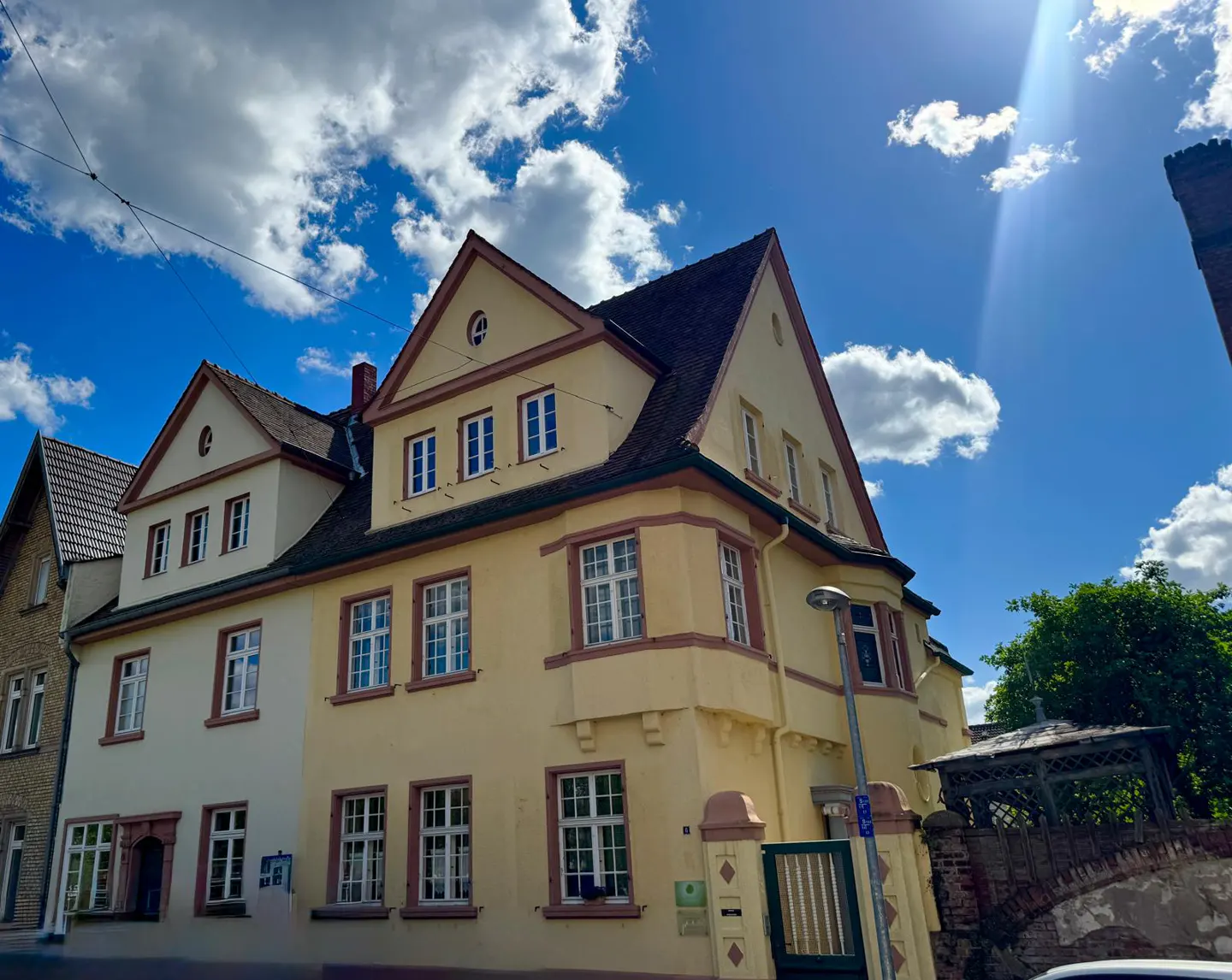 Three-story yellow building with white windows and a dark roof against a blue sky with white clouds.