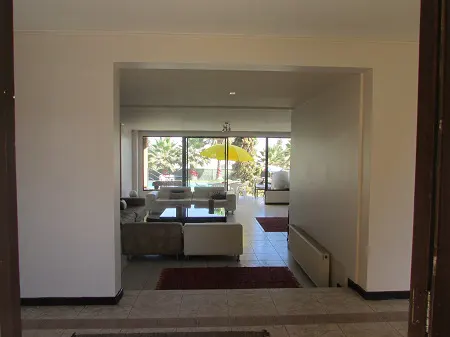View through doorway into a living room with white sofas, a black table, and a yellow umbrella outside.