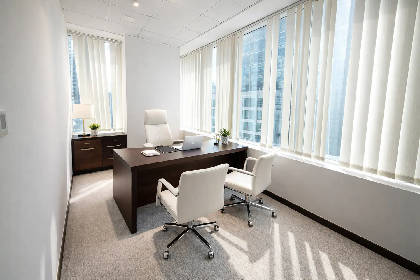 Modern office with a dark wood desk, white leather chairs, and large windows with vertical blinds overlooking a city.
