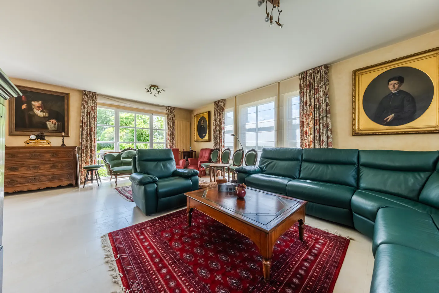Spacious living room with a green leather sectional, matching armchair, wooden coffee table, and red patterned area rug.