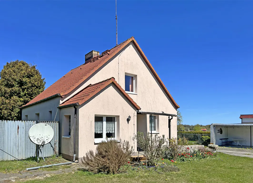 Exterior view of a one-story house with a red tile roof, beige stucco walls, and a satellite dish in the yard.