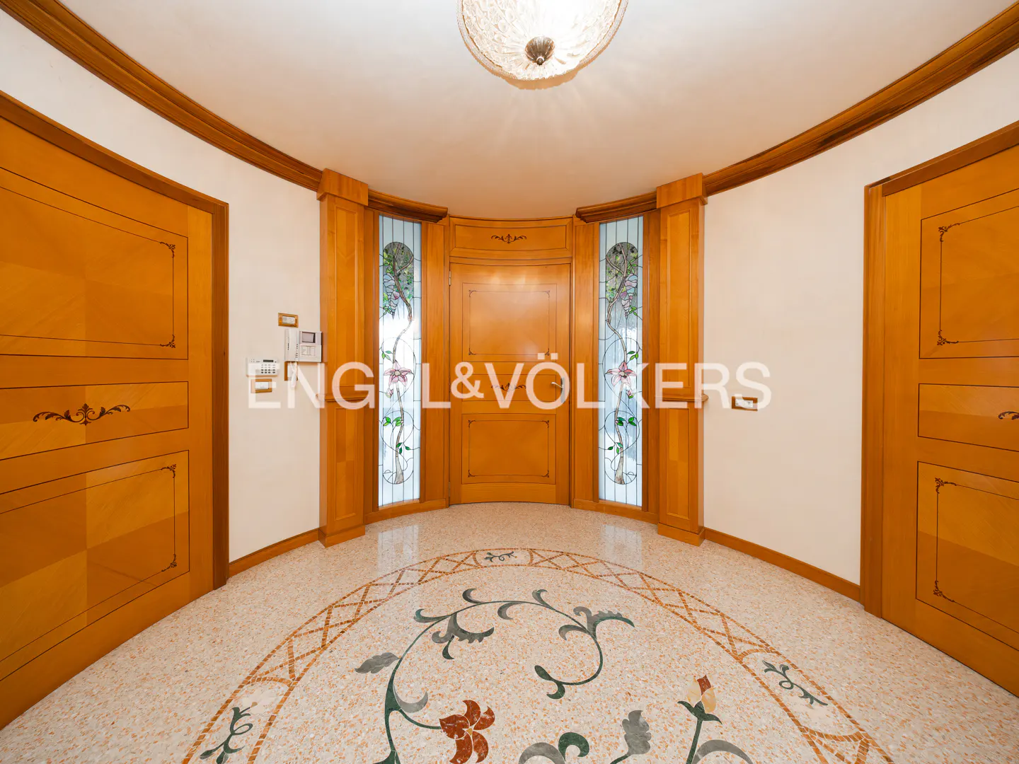 A foyer with a floral mosaic floor, wood doors, and stained glass windows. A light fixture is on the ceiling.