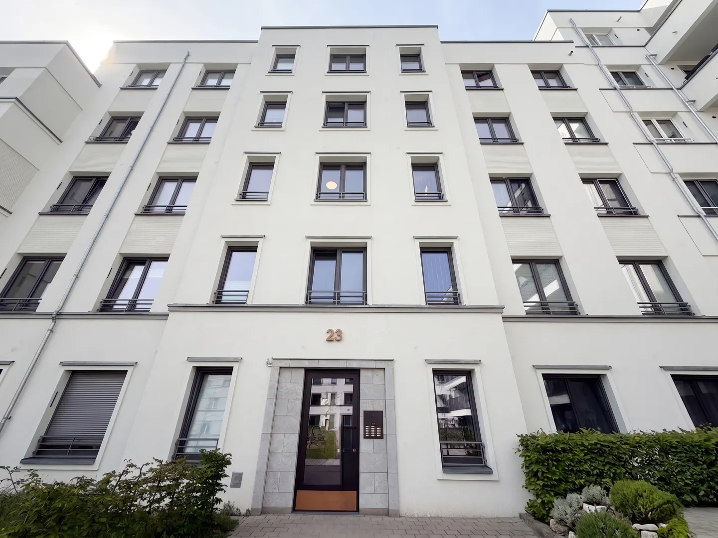 Low-angle shot of a white apartment building with dark-framed windows and the number 23 above the entrance.