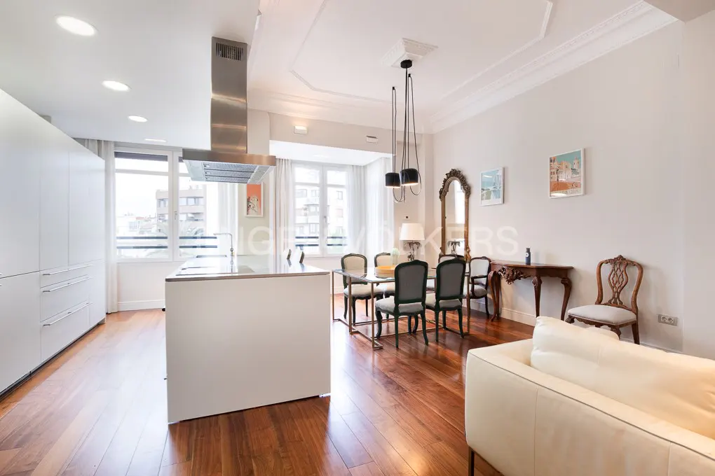 Modern open-plan kitchen and dining area with white cabinets, wooden floors, a dining set, and a cream sofa.