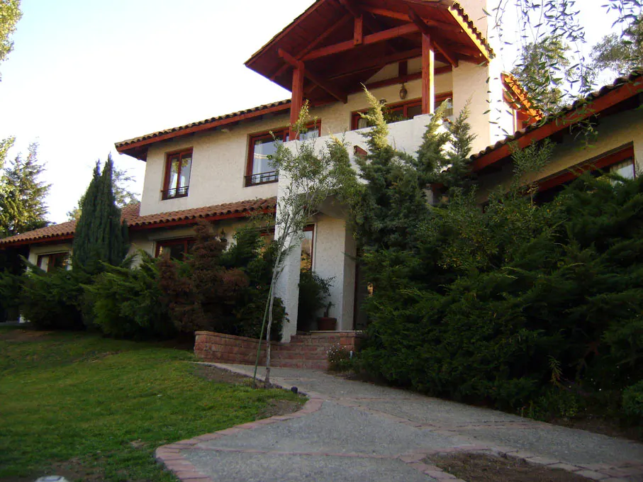 Two-story house with a red-tiled roof, white walls, and a stone walkway leading to the front door. Green bushes surround the house.