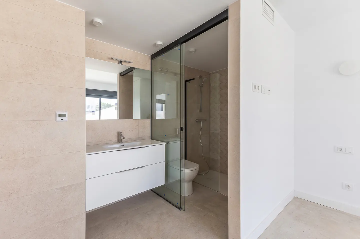 Modern bathroom with a white floating vanity, beige tiled walls, and a glass-enclosed shower with a toilet.