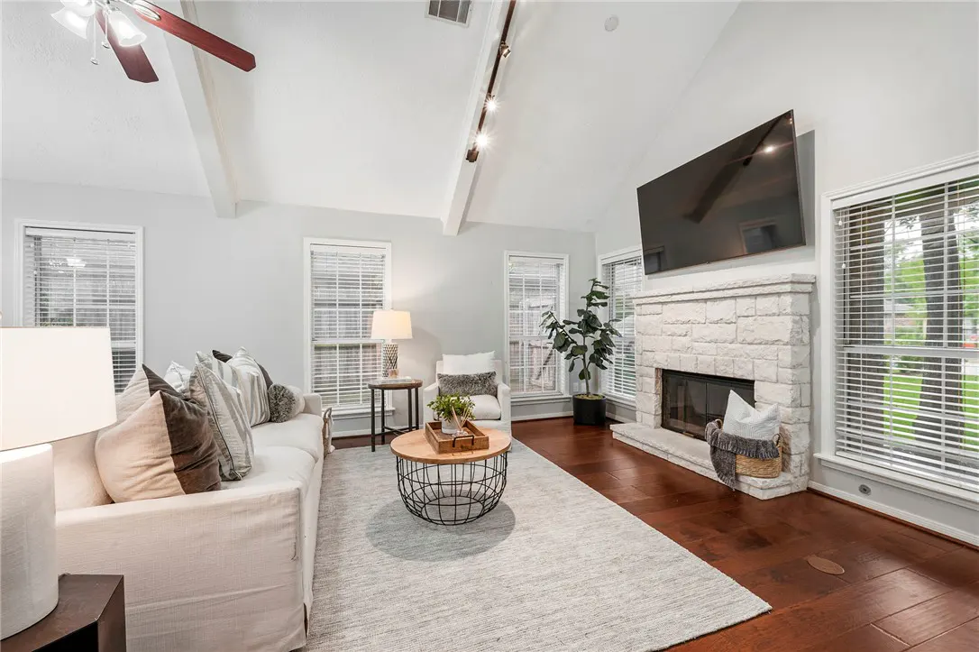 Living room with white sofa, stone fireplace, and dark wood floors. A ceiling fan and track lighting are visible.
