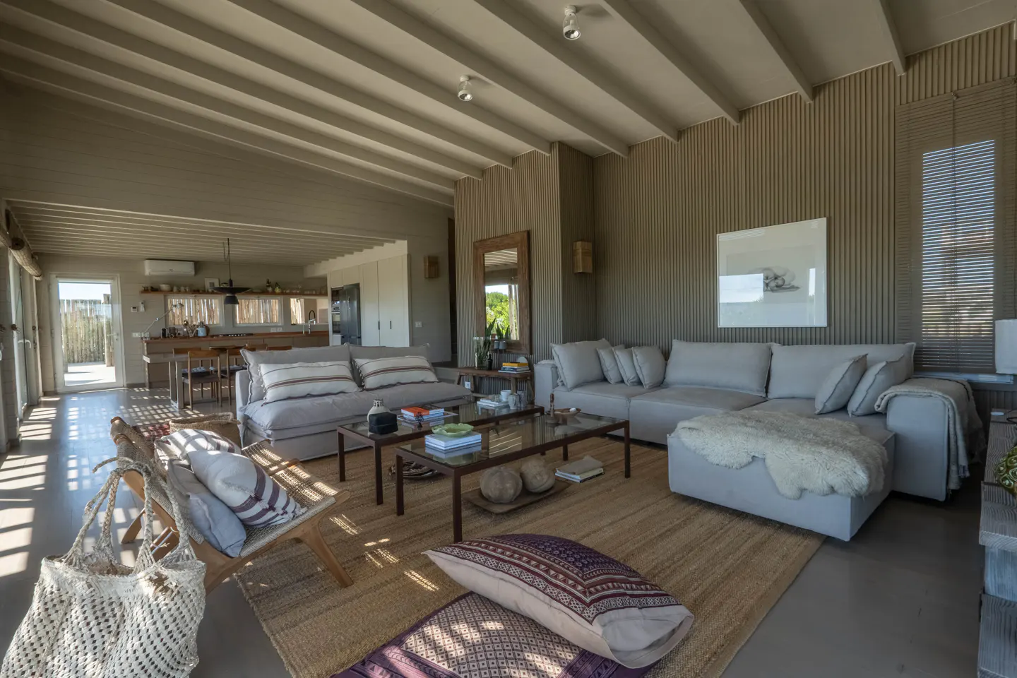 Open-concept living room with gray sofas, wood accents, and a jute rug. Natural light streams in from the windows.