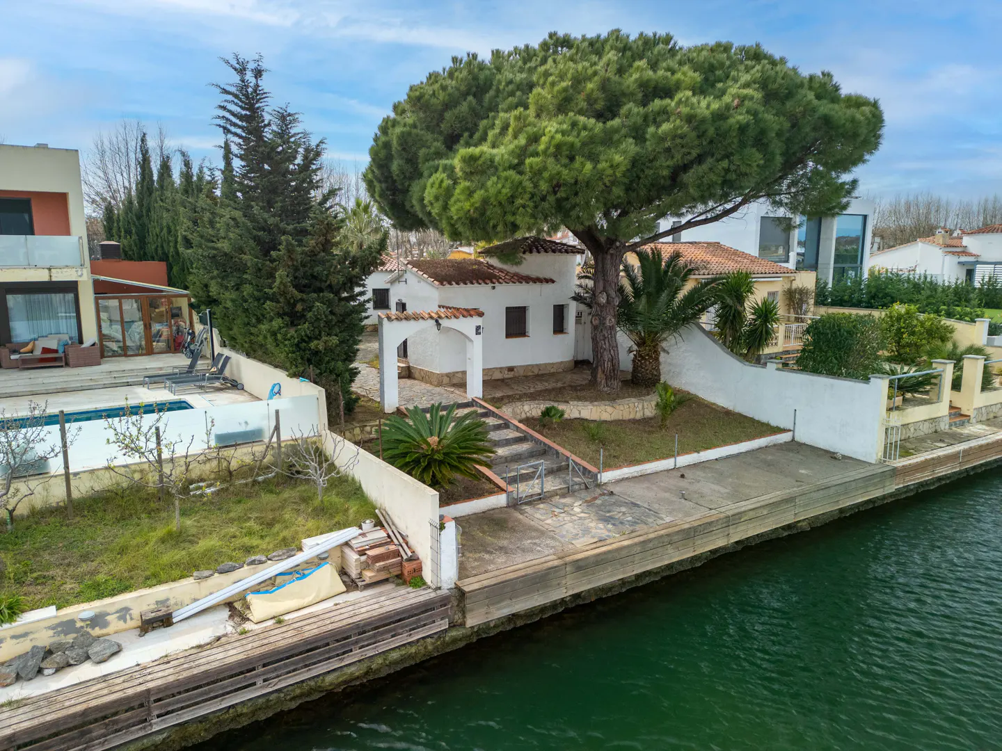 Waterfront home with a large tree. The white house has a red tile roof and is next to a canal.