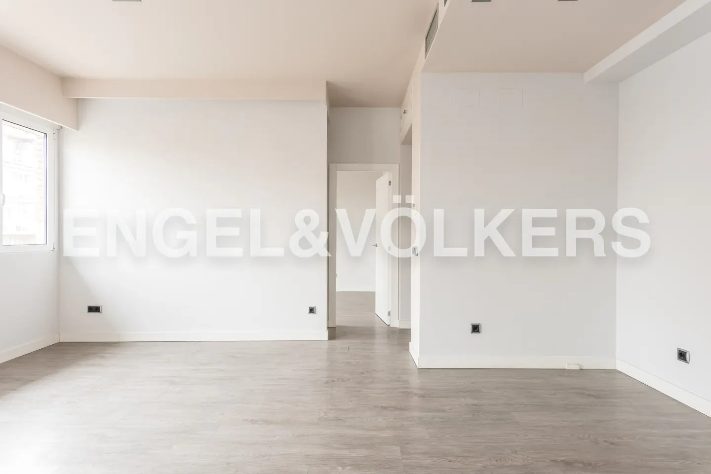 Empty, bright room with white walls, light wood-look flooring, and a doorway leading to another room.