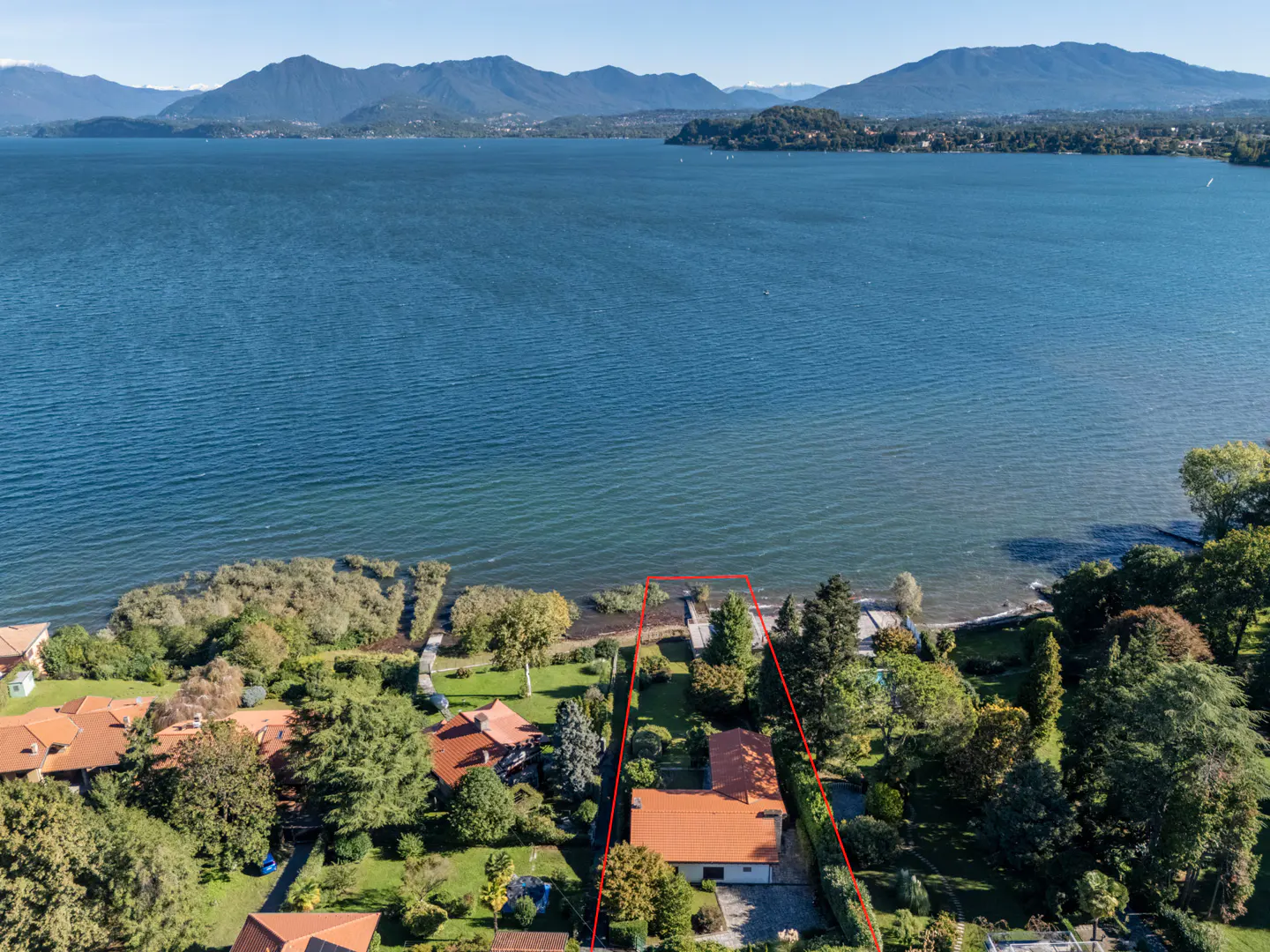 Aerial view of a lakeside property with a red outline, featuring a house with a red roof, green trees, and a blue lake.
