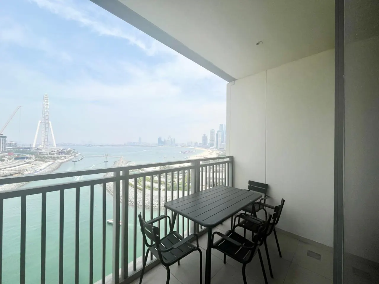 Balcony with a gray table and four chairs overlooking a city skyline and ocean view.