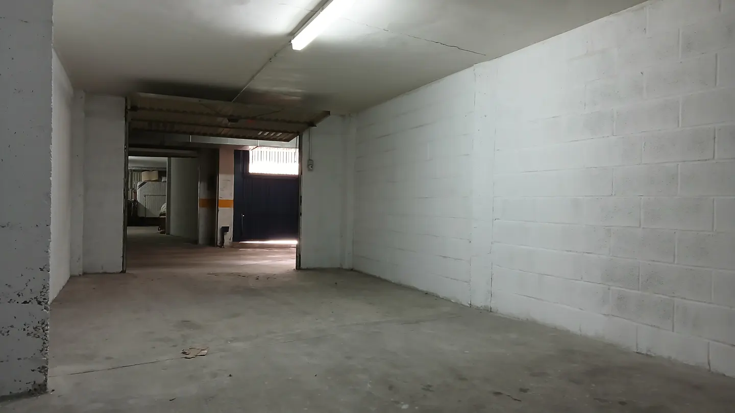 Empty underground parking garage with white concrete block walls, a concrete floor, and a fluorescent ceiling light.