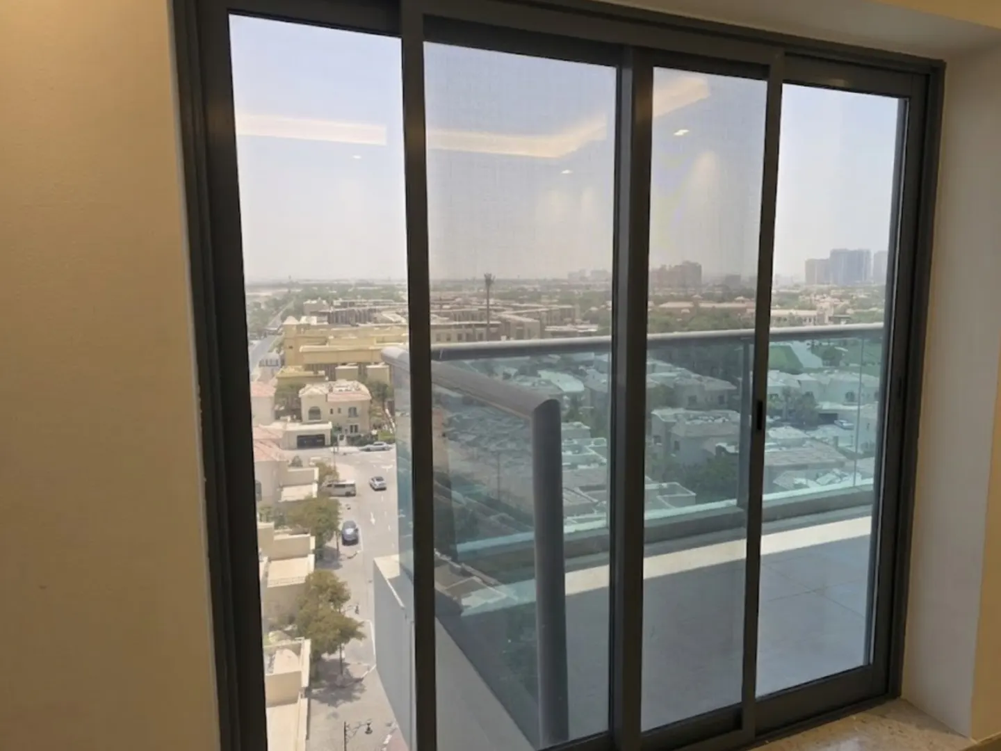 View from a high-rise balcony with sliding glass doors and a gray frame. Cityscape with buildings and streets visible in the background.
