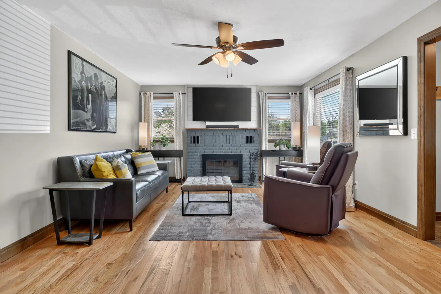A living room with hardwood floors, a gray sofa with yellow pillows, and a gray brick fireplace.