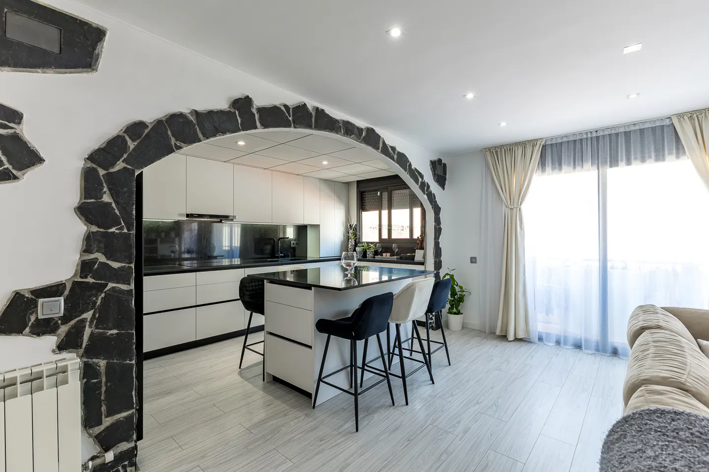 A modern kitchen with a black stone archway, white cabinets, a black countertop, and a kitchen island with stools.