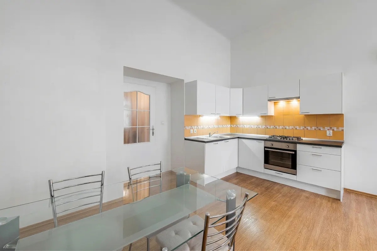 Modern kitchen with white cabinets, yellow tiled backsplash, and a glass dining table with metal chairs on wood flooring.