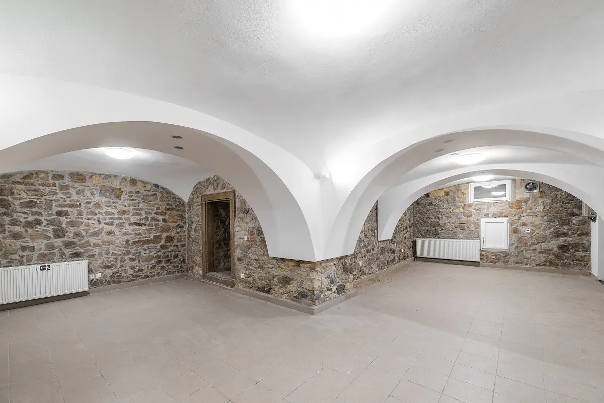 Arched white ceiling over a large room with stone walls, a doorway, and a light gray tiled floor.
