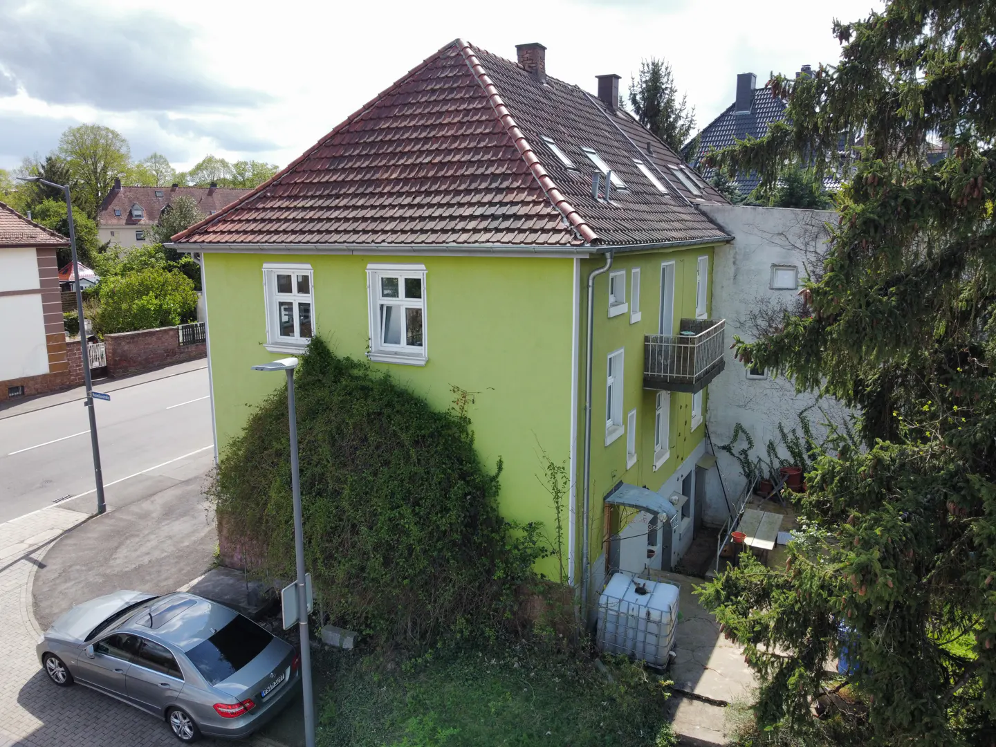 A two-story house with a red tile roof and light green siding. A silver car is parked on the street in front.