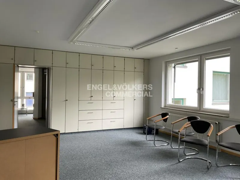 Office space with grey carpet, a wall of white storage cabinets, and three black chairs facing large windows.