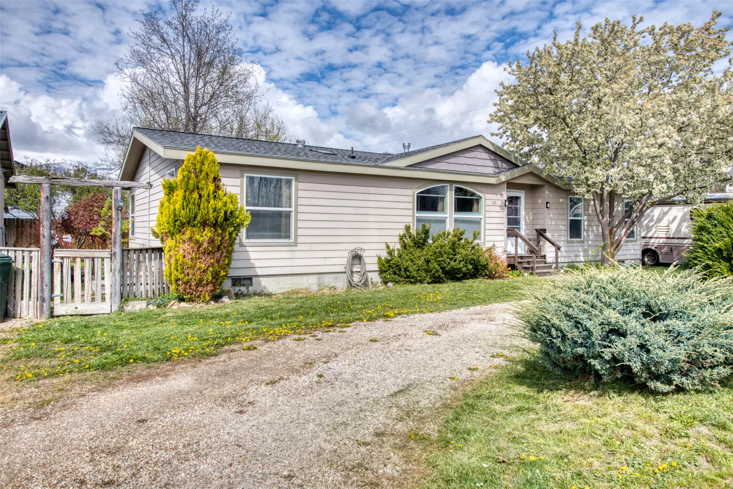 A single-story beige house with a gravel driveway and green lawn on a sunny day.