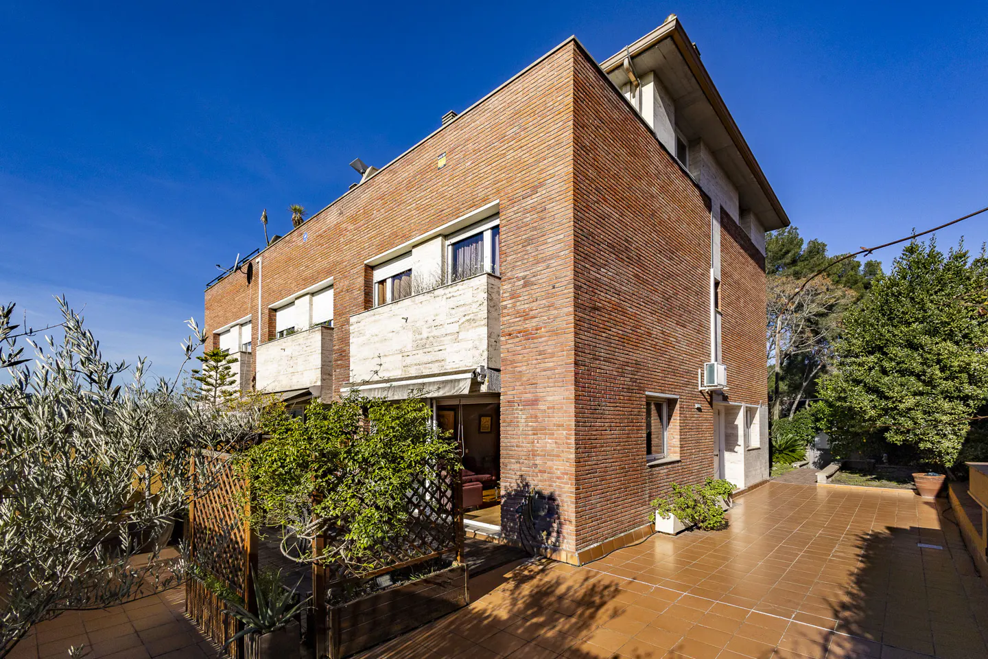 Exterior view of a three-story brick building with balconies and a tiled patio under a clear blue sky.