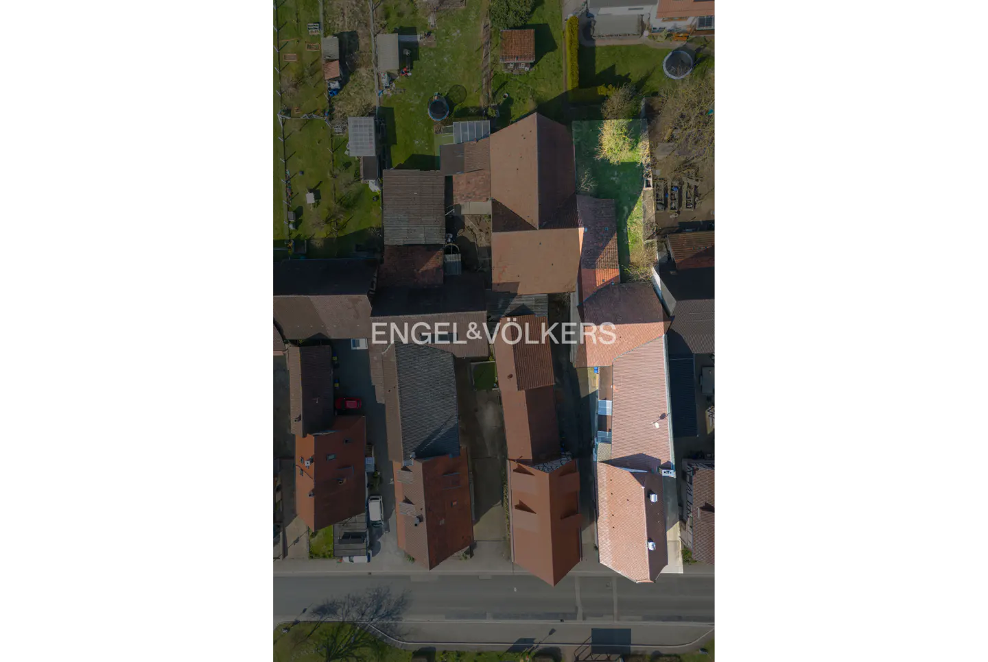 Aerial view of houses with red roofs and green lawns, Engel & Völkers logo in the center.