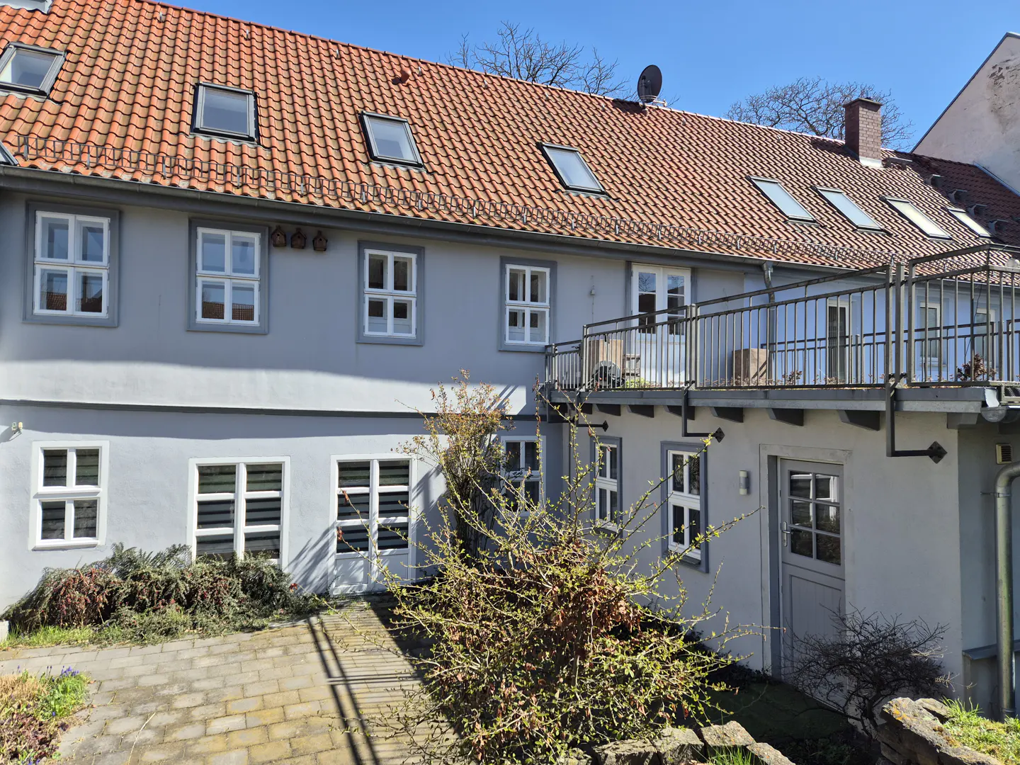 Two-story gray building with a red tile roof and white-framed windows. A balcony with metal railings is on the second floor.