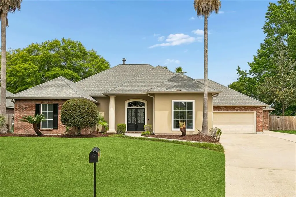 A tan single-story house with a gray roof, brick accents, and a green lawn under a blue sky.