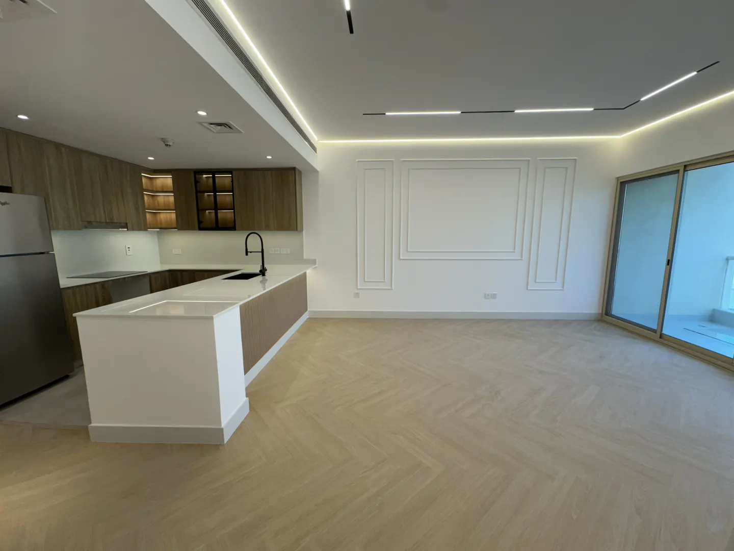 Bright, modern apartment interior with wood cabinets, white island, herringbone floors, and white walls with decorative molding.