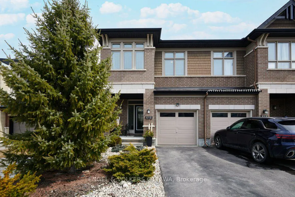 Exterior of a two-story brick townhouse with a beige garage door and a dark blue car parked in the driveway.