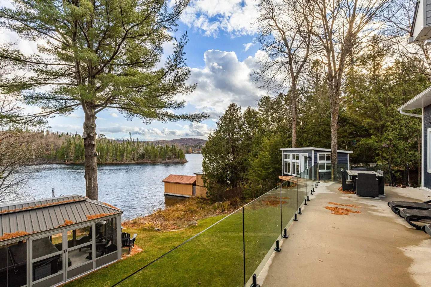 Lake view from a patio with glass railings, a small blue shed, and a covered gazebo on the lawn.