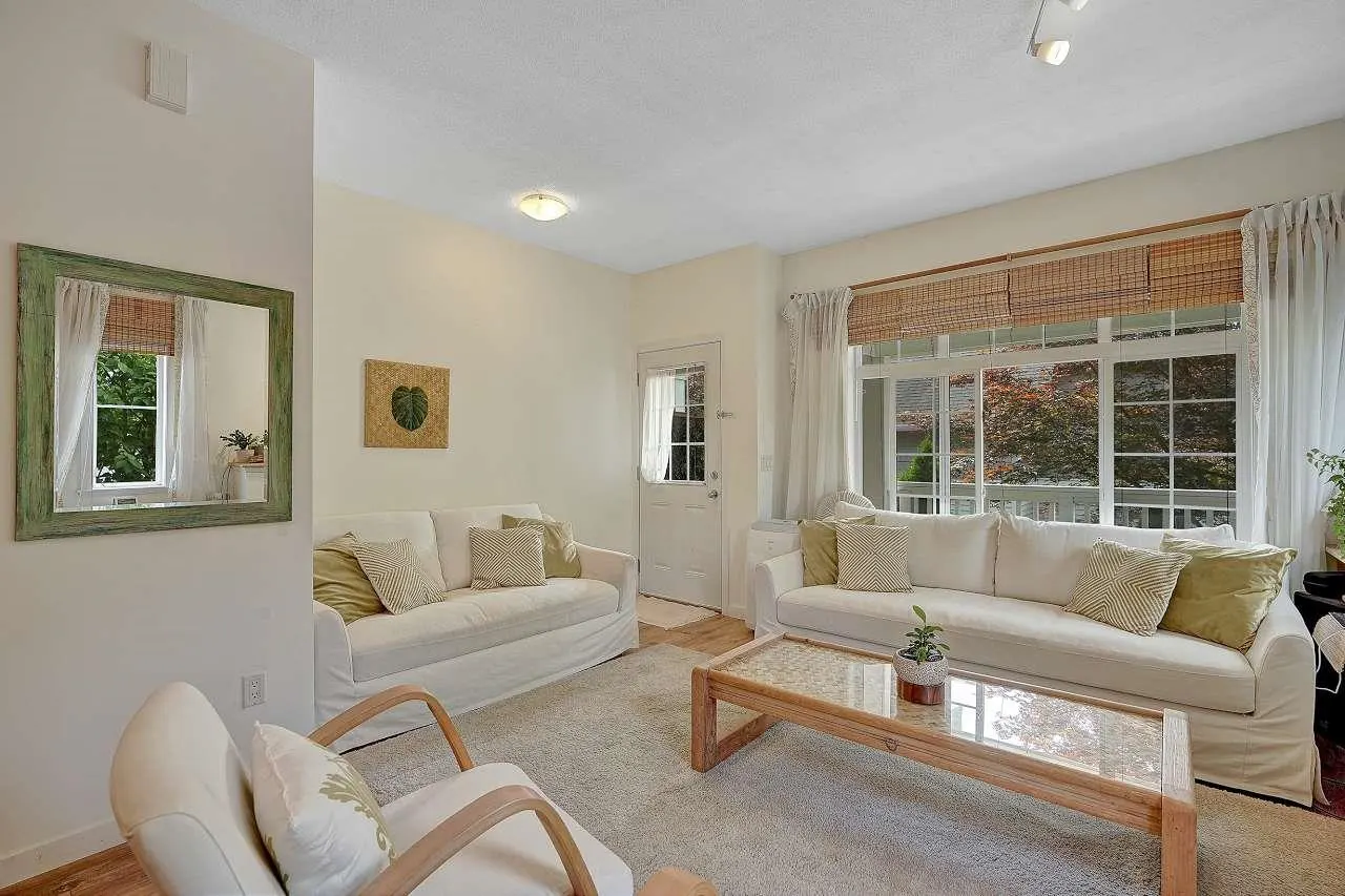 Living room with white sofas, wood-framed glass coffee table, and a green-framed mirror on a cream wall.
