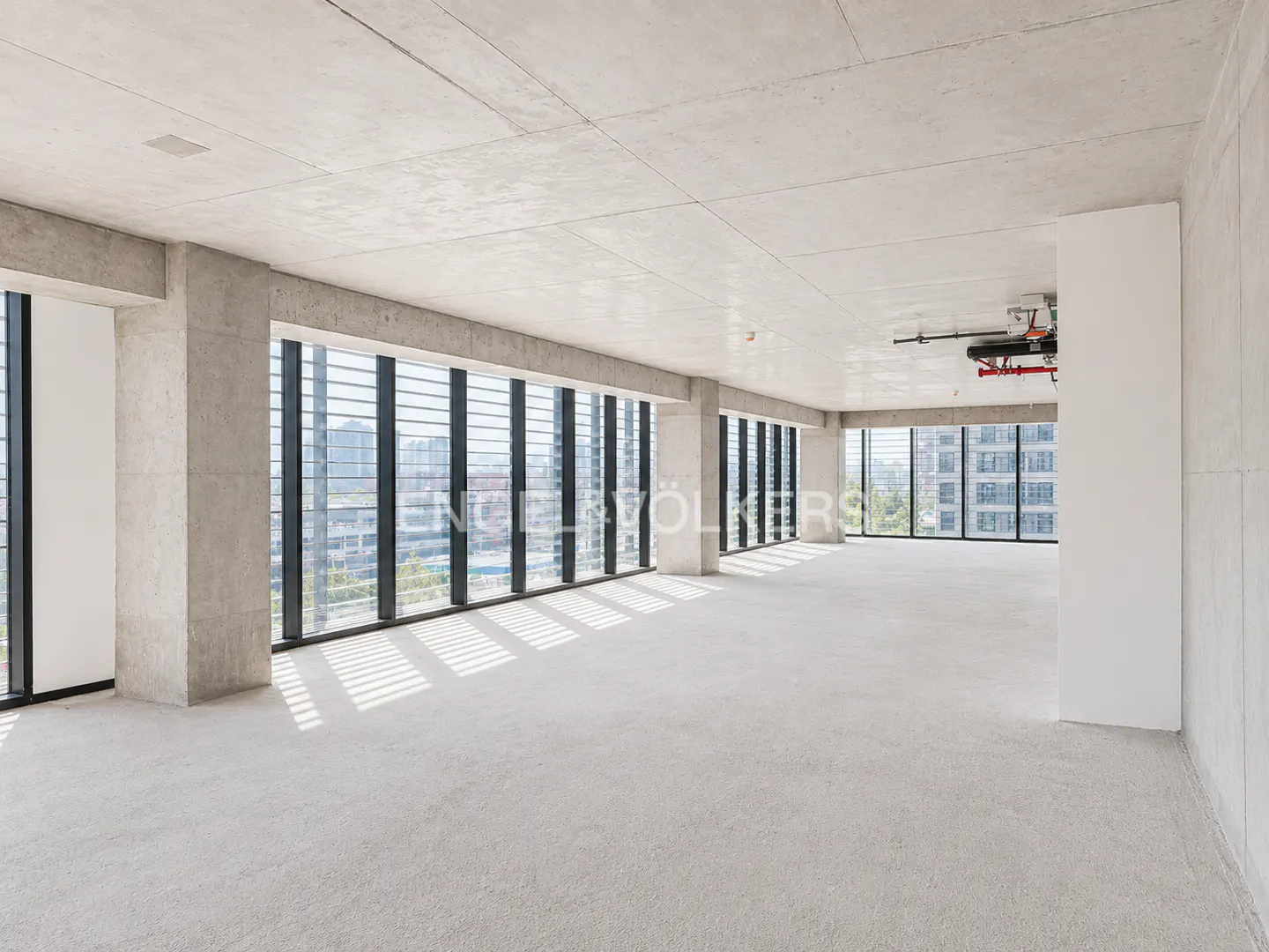 Unfurnished, light-filled room with concrete walls, floor, and ceiling. Large windows with black frames offer city views.